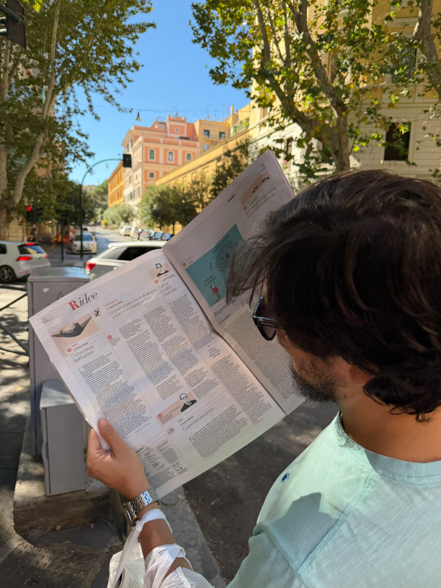 Un lettore sfoglia le pagine culturali de la Repubblica per strada a Roma, con palazzi e platani sullo sfondo